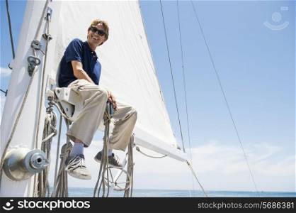 Low angle view of smiling man sitting on yacht boom