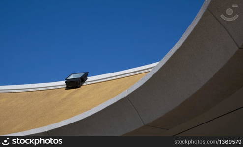 Low angle view of spotlight on top of modern roof in curve pattern against blue clear sky background in sunny day, exterior architecture concept