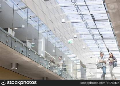 Low angle view of students talking while standing on glass floor at university campus