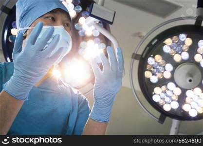 Low angle view of surgeon holding gloved hands up with surgical lights behind him