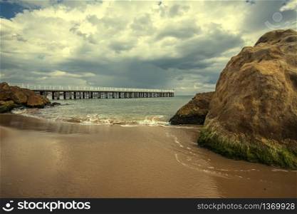 Low angle view of the sea waves with a pier and big rocks on the shore