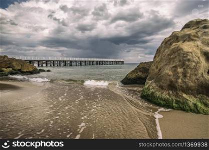 Low angle view of the sea waves with a pier and big rocks on the shore