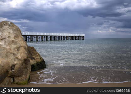Low angle view of the sea with a pier and big rock on shore