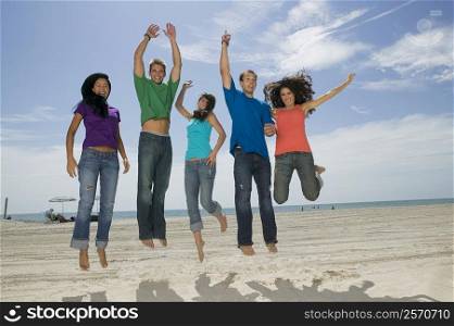 Low angle view of three young women and two young men jumping on the beach