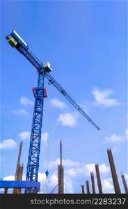 Low angle view of tower crane with foundation pillars and reinforced steel bars against clouds and blue sky in construction site area