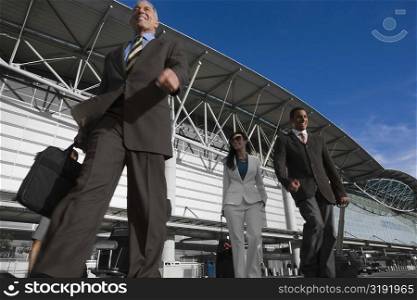 Low angle view of two businessmen with a businesswoman walking outside an airport