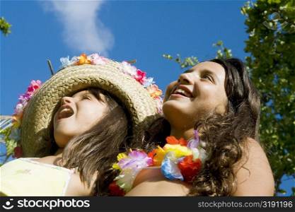 Low angle view of two girls wearing flowers and smiling