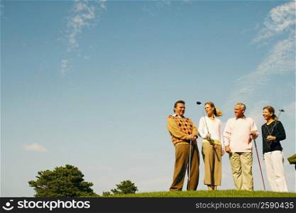 Low angle view of two men and two women holding golf clubs