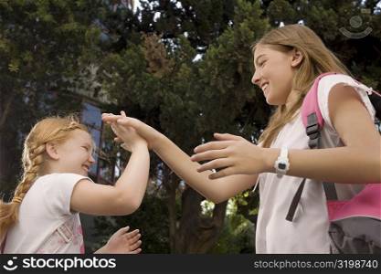 Low angle view of two schoolgirls playing clapping game and smiling