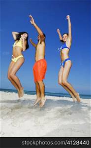 Low angle view of two young women and a young man jumping on the beach