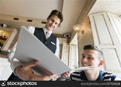 Low angle view of waiter showing menu to male customer in restaurant
