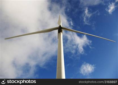 Low angle view of wind turbine against blue sky and clouds.