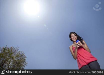 Low angle view of woman text messaging on a sunny day
