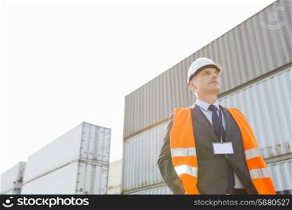 Low angle view of worker standing against cargo containers in shipping yard