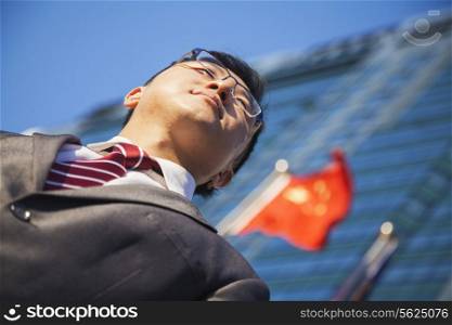 Low angle view of young businessman in front of a building with Chinese flag in the background
