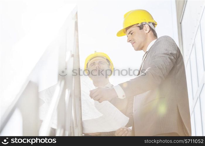 Low angle view of young businessman in hard hats reviewing blueprint on stairway