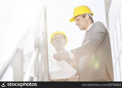 Low angle view of young businessman in hard hats reviewing blueprint on stairway