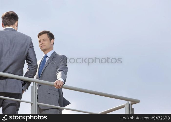 Low angle view of young businessman looking at coworker against clear sky