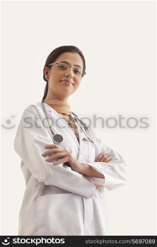 Low angle view of young confident female doctor standing against white background