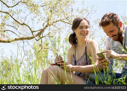 Low angle view of young couple sitting looking down at smartphone smiling