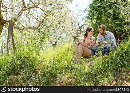Low angle view of young couple sitting on hill holding smartphone