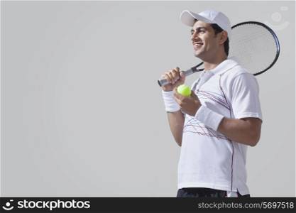 Low angle view of young man holding tennis racket and ball isolated over gray background