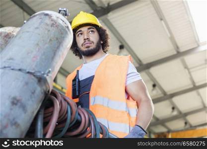 Low angle view of young manual worker moving gas cylinder in metal industry