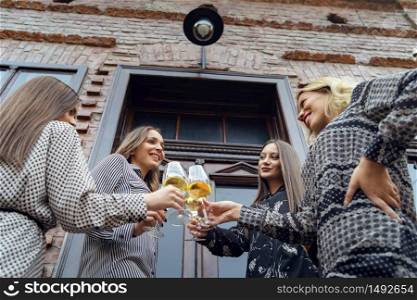 Low angle view on four beautiful young caucasian women females only friends standing by the door of old house holding glasses with wine toasting celebrating wearing summer dresses