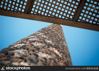 Low angle view on wooden shade of seating bench with pebble stone column.