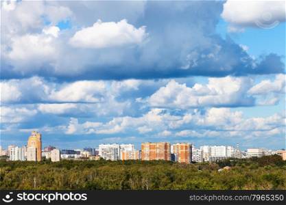 low blue clouds over green forest and city in summer