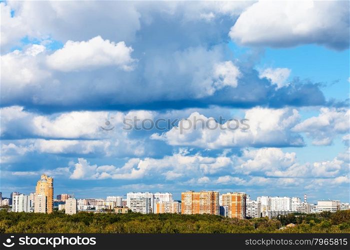 low blue clouds over green woods and apartment buildings in summer