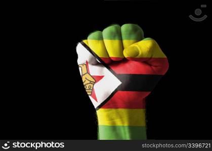 Low key picture of a fist painted in colors of zimbabwe flag