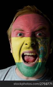 Low key portrait of an angry man whose face is painted in colors of bolivian flag