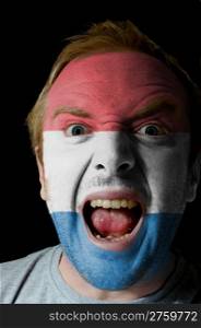 Low key portrait of an angry man whose face is painted in colors of netherlands flag