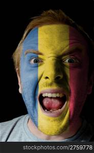 Low key portrait of an angry man whose face is painted in colors of romanial flag