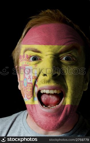 Low key portrait of an angry man whose face is painted in colors of spain flag