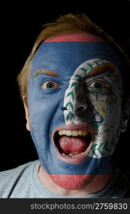 Low key portrait of an angry man whose face is painted in colors of belize flag