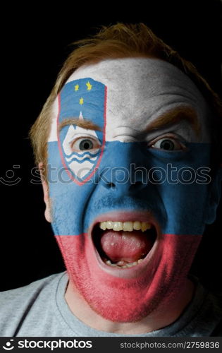 Low key portrait of an angry man whose face is painted in colors of slovenia flag