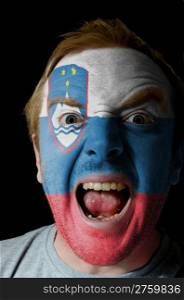 Low key portrait of an angry man whose face is painted in colors of slovenia flag