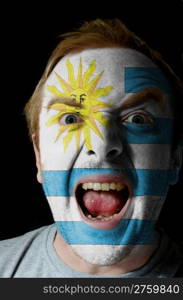 Low key portrait of an angry man whose face is painted in colors of uruguay flag