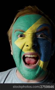 Low key portrait of an angry man whose face is painted in colors of brazilian flag