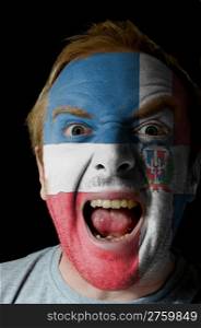 Low key portrait of an angry man whose face is painted in colors of dominican republic flag