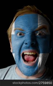 Low key portrait of an angry man whose face is painted in colors of finland flag