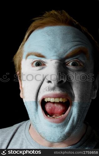 Low key portrait of an angry man whose face is painted in colors of argentinian flag
