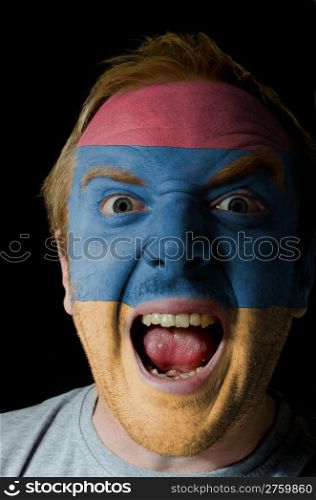 Low key portrait of an angry man whose face is painted in colors of armenian flag
