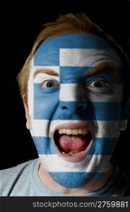 Low key portrait of an angry man whose face is painted in colors of greece flag