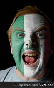 Low key portrait of an angry man whose face is painted in colors of mexico flag