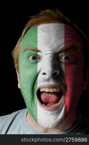 Low key portrait of an angry man whose face is painted in colors of italian flag