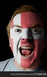 Low key portrait of an angry man whose face is painted in colors of denmark flag
