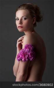 low key portrait of young blond naked woman with flower bouquet around her arm